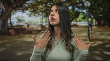 Uzun koyu renk saçlı genç İspanyol kadın sıcak bir öğleden sonra güneşli bir öğleden sonra parkta ellerini uzattı..