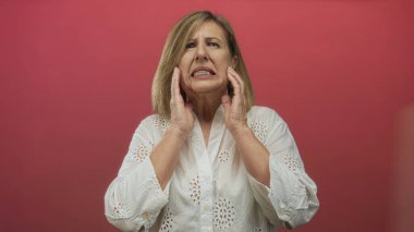 Kadın, acı verici bir ekşilik sergilerken iki eliyle kırmızı bir stüdyo duvarına çıplak yanak bastırıyor; diş ağrısı rahatsızlık veriyor..