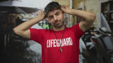 Kırmızı cankurtaran gömleği giyen adam parmaklarını sokak kafesinin terasına koyar..