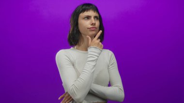 Mor stüdyoda elleri çenesinde beyaz, uzun kollu bir bluz giyen İspanyol genç bir kadın. İç gözlem şüphesi..