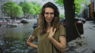 Kadın, Amsterdam 'da kanal suyunun yanına elini koyuyor demirli tekneler ve yapraklı ağaçlarla; neşe.