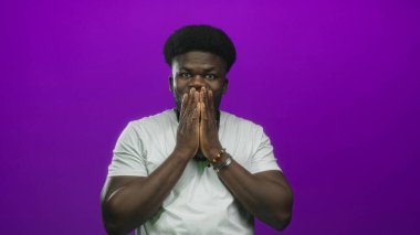 Mor stüdyoda eli ağıza hareket eden, boncuklu kolyesi ve beyaz tişörtü olan genç Afro-Amerikalı bir adam..