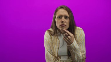 Stüdyoda parmakları çenesinde morumsu arka plana bakan, çizgili gömlek ve beyaz bluz giyen, düşünceli, şaşı bakışlı bir kadın..