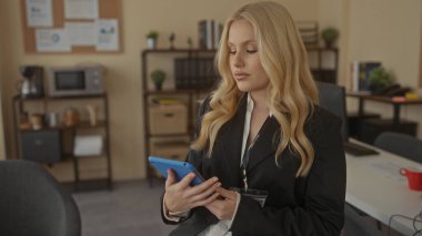 Ofis ortamında tablet kullanan sarı saçlı bir kadın, raflar, kitaplar ve bitkilerle çevrili, profesyonel ve odaklanmış bir çalışma ortamı sağlıyor..