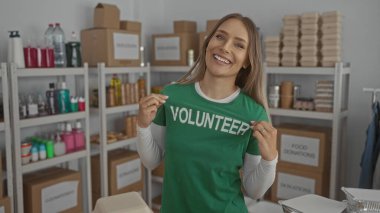 Bağış merkezinde gülümseyen bir kadın gönüllü gömleği giyip evin içinde kutular ve malzemelerle çevrili bir şekilde hayır kurumunun mekanında olumlu ve yararlı bir atmosfer yakalamış.