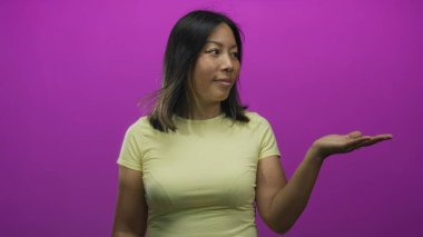 Avuç içini mor stüdyoda tutan, soluk sarı tişört giyen ve kameraya bakan tarafsız yüzlü, meraklı açıklık.