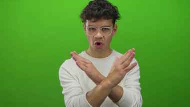 Gözlüklü ve beyaz gömlekli İspanyol genç adam yeşil bir stüdyo önünde inkar jesti olarak kollarını çapraz yapar. Reddetme.