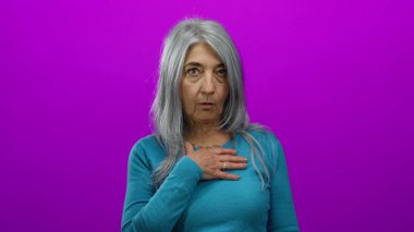 Gri saçlı, mavi süveter giyen son sınıf öğrencisi kadın, göğsünde duygu taşıyan, soyutlanmış pembe arka plana şaşırdığını ifade ediyor..