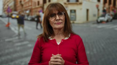 Kırmızı kazaklı yaşlı İspanyol kadın hareketleriyle kalabalık bir şehir caddesinde canlı şehir yaşamını resmediyor..