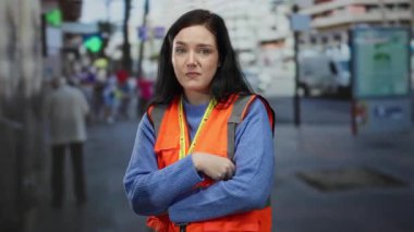 Yoğun bir sokakta duran turuncu yelek giyen gönüllü bir kadın, bir topluluk ortamında özveri ve farkındalık sergiliyor..