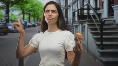 Park halindeki arabaların ve tuğladan evlerin arasında sokak kaldırımını işaret eden ve muffin tutan kadın..