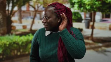 Kulaktan kulağa dikkatle dinleyen, yeşil süveter giyen, ağaçlarla çevrili ve şehir dışında yaşayan, canlı kırmızı örgüler sergileyen bir kadın..