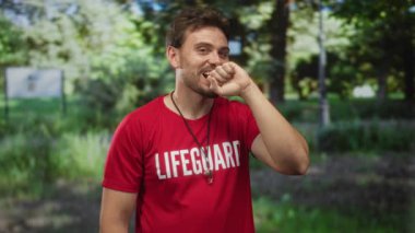 Kırmızı gömlekli bir adam orman ortamında ıslık kolyesiyle yumruğunu ısırır; görev tetikte olma yorgunluğu.