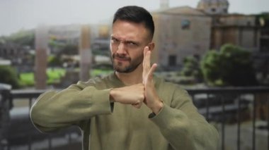 Yeşil kazaklı İspanyol bir adam, İtalya 'daki antik Roma harabelerinin arka planına sergilenen ve kültürel mirasını gözler önüne seren yumruğuyla avcuna vurarak kararlı bir hareket yapıyor..