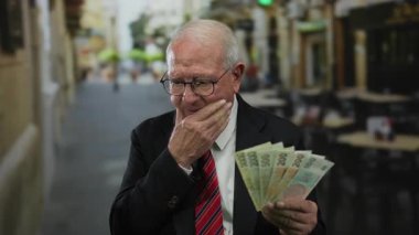 Takım elbiseli kıdemli bir adam, elinde Czech Koruna banknotları ile caddedeki açık hava restoranının terasında kafa yoruyor..