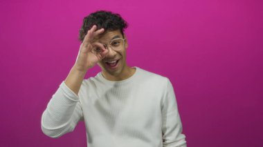 Gözlüklü bir adam mor stüdyo ortamında parmaklarıyla işaret işareti yapıyor. Tamam onaylandı..