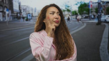 Pembe gömlekli kadın, şehir caddesinde yukarı bakan tramvay izleriyle yanak yanağa işaret ediyor. Düşünceli bir şüphe..