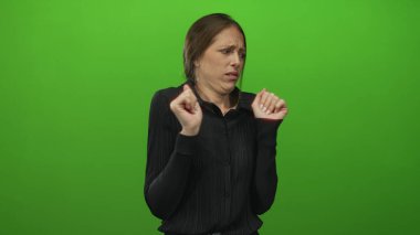 Avuçlarını kaldırmış ve parmakları bükülmüş genç bir kadın yeşil bir stüdyoda ekşitme ile geri çekilme; iğrenme kaçınma huzursuzluğu.