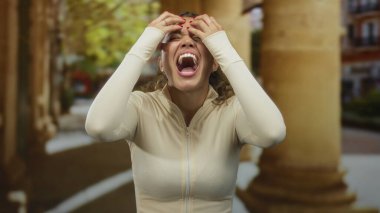 Eski bir kasaba ortamında hayal kırıklığını ifade eden bir kadın, krem bir bluz giyiyor ve başını tutuyor, arka planda bulanık tarihi mimariyle çevrili..