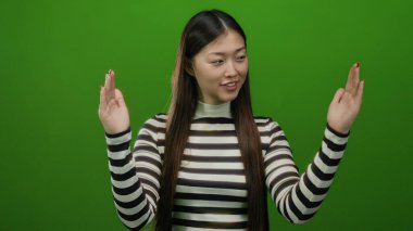 İzole edilmiş yeşil arka planda, çizgili gömlekli, neşeli bir ifade sergileyen, Asyalı özelliklerini ve modern moda anlayışını vurgulayan bir kadın..