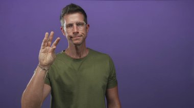 Yeşil tişörtlü, gözlüklü, mor stüdyo ortamında parmaklarını çimdikleyen bir adam..