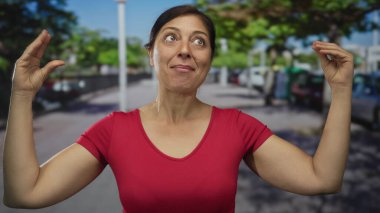 Kırmızı gömlekli kadın çıplak kollarını kaldırır ve parmaklarını sokakta çimdikler; konsantrasyon hassasiyeti dikkat.