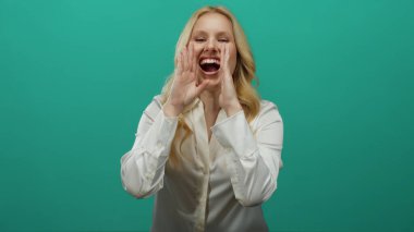 Sarışın genç bir kadın neşeli bir şekilde yeşil bir arka plana gülüyor. Bulaşıcı bir gülümsemesi var. Rahat bir atmosferde..