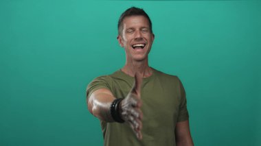 El sıkışmak için sağ elini uzatan ve zeytin tişörtü ve bilezikleriyle bir deniz mavisi stüdyosunda gülümseyen adam; dostça karşılama.