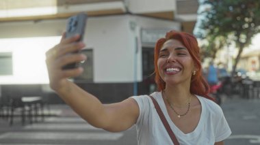 Kadın akıllı telefonuyla selfie çekiyor, kolu kafenin yanındaki yaya geçidinde uzanıyor ve scooter park ediyor..