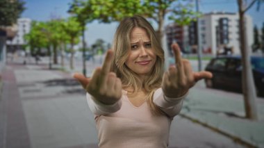 Kırışık kaşlı sarışın kadın, şehir sokağının köşesinde orta parmaklarını sallıyor, başkaldırı isyanının hüsranı..