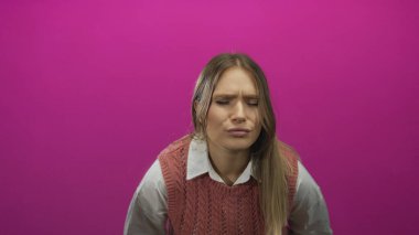 İzole edilmiş pembe arka planda mide rahatsızlığını ifade eden, sarışın saçlarını gösteren ve neşeli bir ortamda acı çeken bir kadın..