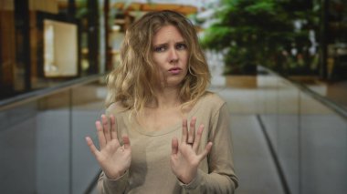 Kadın alışveriş merkezinin içinde engelleyici bir duruş sergiliyor. Sarışın genç bir denek iç mekanda endişeli ve somurtkan görünüyor..