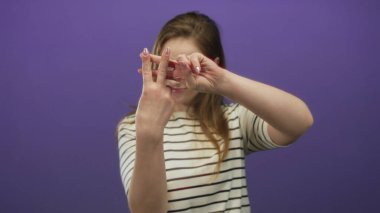 Çizgili gömlek giyen bir kadın mor bir stüdyoda parmaklarıyla hashtag jesti oluşturuyor; neşeli bir bağlantı.