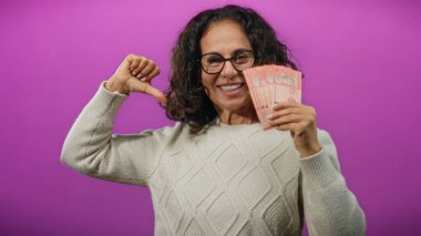 Beyaz süveterli bir kadın, elinde mor arka planda Malezya bankaları tutarken gülümsüyor..