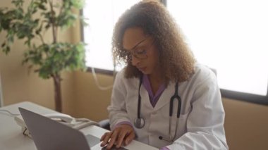 Klinikte masa başında otururken dizüstü bilgisayarında steteskop tipli beyaz önlüklü kadın doktor; azim çözümüne odaklan.