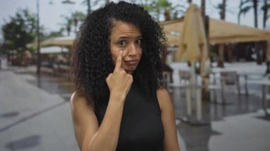 Latin kökenli genç bir kadın güneş ışığıyla aydınlanan terasta gözüne dokunuyor..