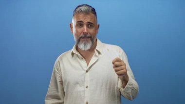 Mavi stüdyo ortamında kredi kartı tutan ve avuç içi kaldıran sakallı orta yaşlı bir adam; şüphecilik uyarısı.