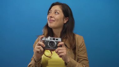 Orta yaşlı İspanyol kadın, mavi profesyonel stüdyo ortamında çıplak elleriyle klasik kamera tutuyor..