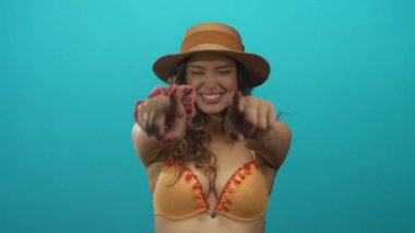 Stüdyo ortamında hasır şapka ve bikini giyen ve gülümseyen bir kadın. Eğlenceli bir davet..