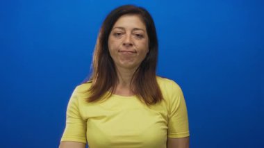 Güzel ışıklandırılmış parlak mavi stüdyo duvarına el sallayan kadın; sıcak kalpli karşılama teması.