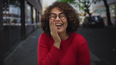 Bir şehir sokak sahnesinde elleri yanağında ve geniş bir gülümsemeyle gülen bir kadın; mutluluk..