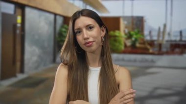 Çapraz kollu genç İspanyol kadın modern bir bina girişinde kolsuz bluz giyiyor..