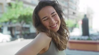 Kadın yüzü rüzgarlı saçlar ve eğimli omuz ile geniş gülümseyerek gün ışığında sokakta; kaygısız sevinç.