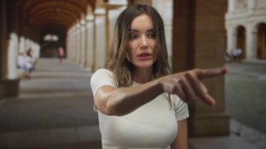 Genç İspanyol kadın, eski kasabadaki kaldırım taşı caddesindeki kemerli koridor binasını işaret ediyor..