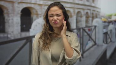 Roma 'da, sembolik kolezyumun yanında dikilen bir kadın, yanağında bir elle acıyla İtalyan çevresindeki İspanyol özelliklerini vurgulayarak, kendini rahatsız hisseder..