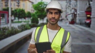 Beyaz tişört ve neon yelek ile sokağa tablet tıklatan insan mühendisliği; konsantrasyon planlama verimlilik.