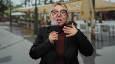 Mikrofonlu kadın muhabir şehirdeki hareketli bir restoran terasında tutkuyla konuşuyor.