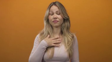 Sarışın kadın, fotoğraf stüdyosunda parmak göğse, kaşlarını kaldırmış ve dudaklarını büzmüş bir şekilde işaret ediyor..