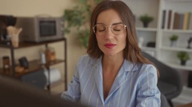 Gözlüklü kadın ofis binasında parmak ekrana işaret ediyor; verimlilik hırsına odaklanıyor.