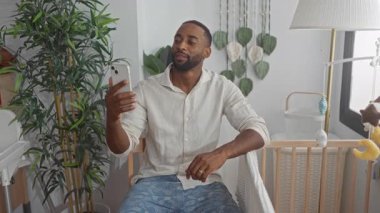 Bir binanın içinde bebek beşiğinin yanında oturan bir adam ekrana bakıyor. Babalık bağı kuruyor..